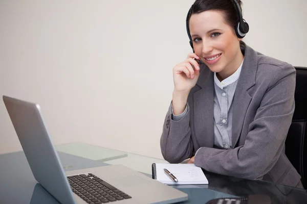 Mujer de negocios sonriente con auriculares en su computadora portátil —  Fotos de Stock