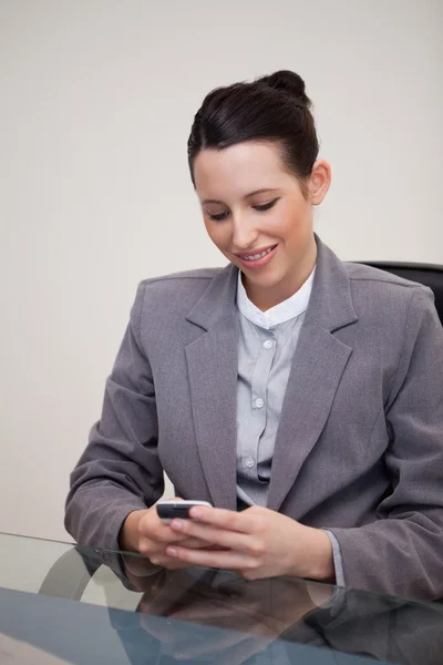 Leende affärskvinna sitter bakom skrivbord skriva ett textmeddelande — Stockfoto