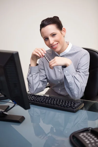 Uśmiechnięta kobieta z pióra siedzi przy biurku — Zdjęcie stockowe