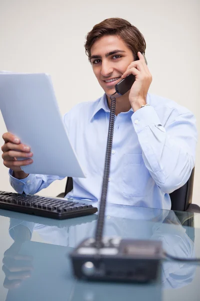 Smiling businessman holding paperwork while on the phone — Stock Photo, Image