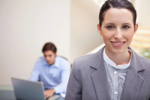 Smiling businesswoman with colleague working on his laptop behin — Stock Photo, Image