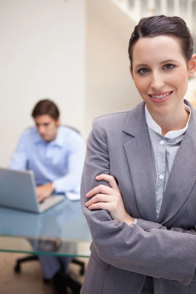 Glimlachende zakenvrouw met collega op zijn laptop achter haar — Stockfoto