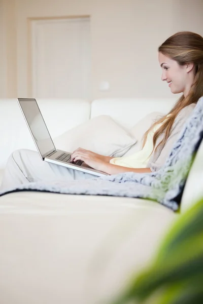 여자는 소파에 앉아 그녀의 노트북의 측면 보기 — 스톡 사진