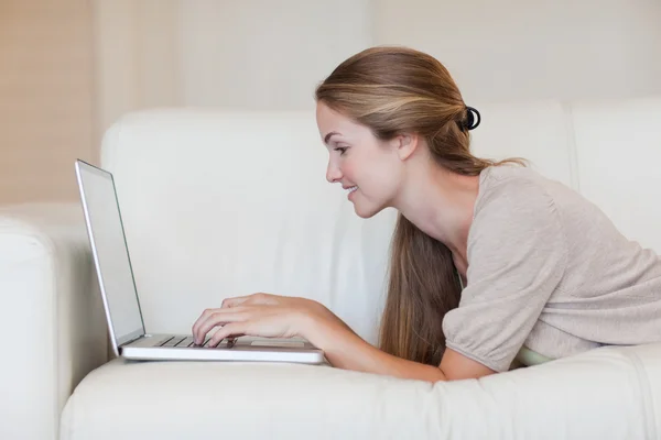 Seitenansicht einer Frau, die mit ihrem Laptop auf dem Sofa liegt — Stockfoto
