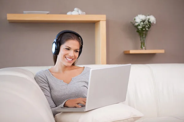 Mulher sorridente com fones de ouvido e laptop no sofá — Fotografia de Stock