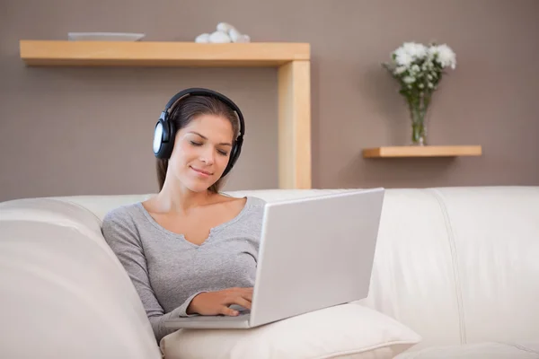 Frau mit Laptop und Kopfhörer auf dem Sofa — Stockfoto