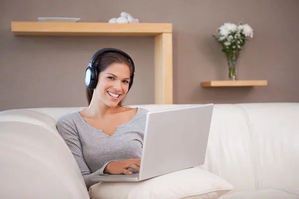 Femme avec ordinateur portable et écouteurs sur le canapé — Photo