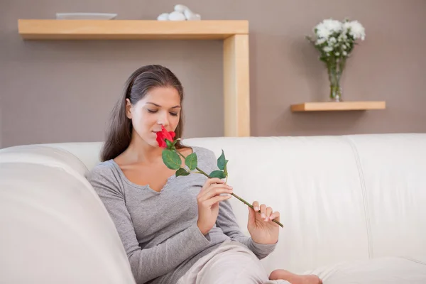 Femme sur le canapé sentant sur une rose rouge — Photo