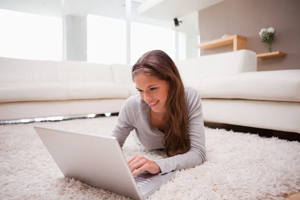 Donna sdraiata con laptop sul tappeto — Foto Stock