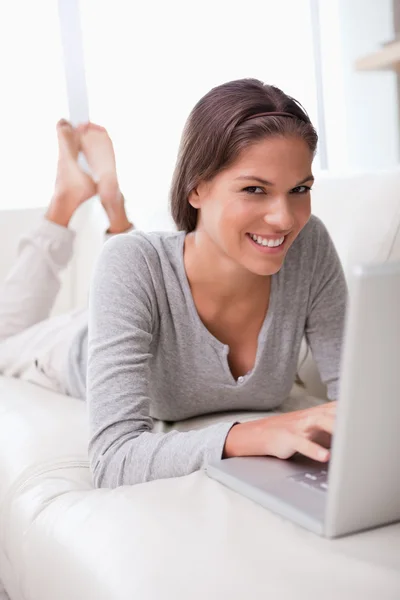 Lachende vrouw met laptop op de bank liggen — Stockfoto