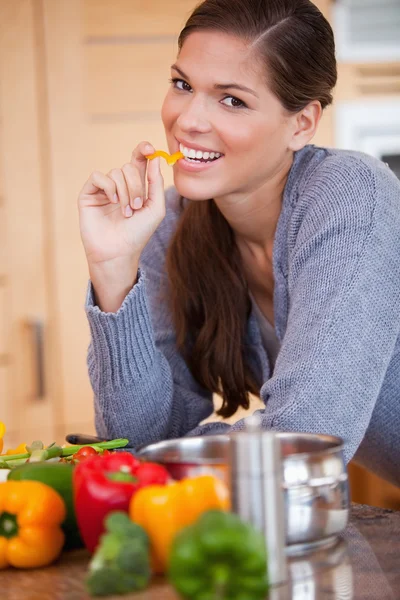 Smiling woman eating a bell pepper in the kitchen — Stock Photo, Image