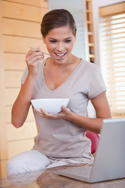 Kvinna äta spannmål vid sin laptop — Stockfoto