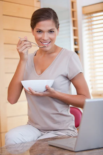 Kvinna med en skål med flingor bredvid hennes laptop — Stockfoto