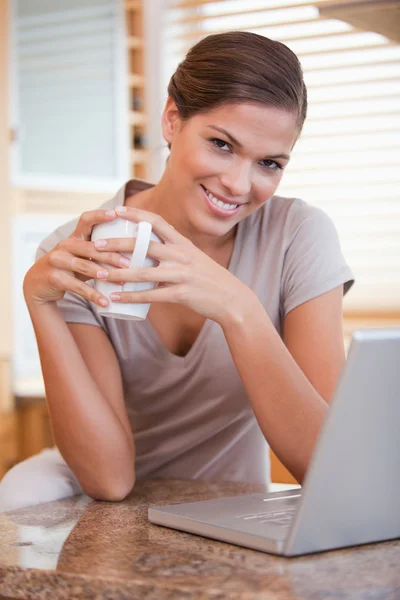 Lachende vrouw met koffie en laptop in de keuken — Stockfoto