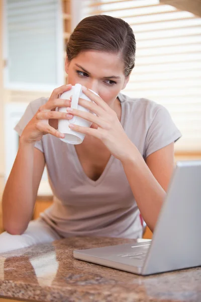 Mujer tomando un sorbo de café junto a su portátil —  Fotos de Stock
