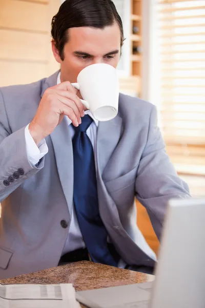 Zakenman neemt een slokje koffie naast zijn laptop — Stockfoto