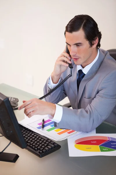 Uomo d'affari che parla al telefono mentre lavora alle statistiche — Foto Stock