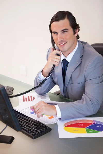 Χαμογελώντας επιχειρηματίας στο τηλέφωνο εργασίας για τις στατιστικές — Φωτογραφία Αρχείου