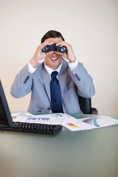 Uomo d'affari alla sua scrivania guardando attraverso il binocolo — Foto Stock