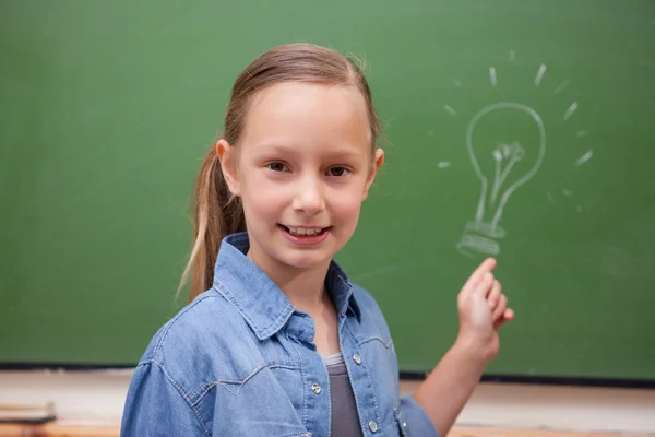 Écolière souriante pointant une ampoule — Photo
