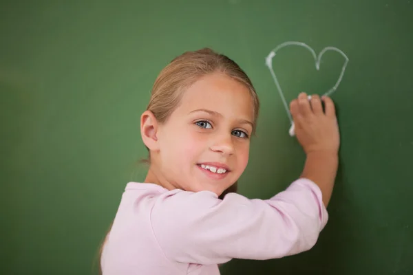 Smiling schoolgirl drawing a heart — Stock Photo, Image