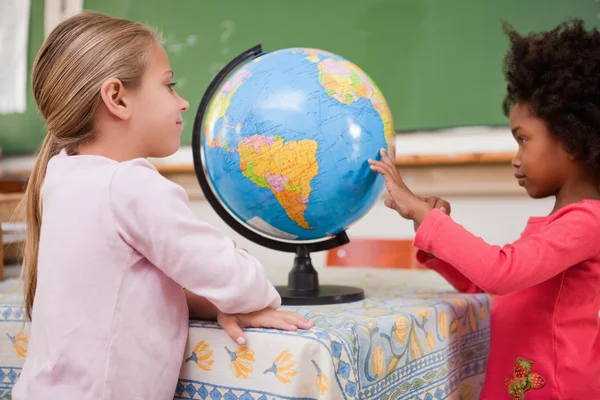 Lachende schoolmeisjes kijken naar een globe — Stockfoto