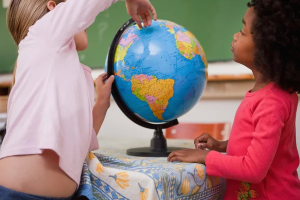 Cute little schoolgirls looking at a globe — Stock Photo, Image
