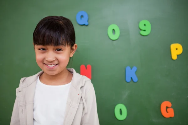Smiling schoolgirl posing in front of a blackboard — Stock Photo, Image
