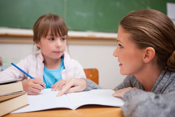 Školačka psaní chvíli její učitel mluví — Stock fotografie