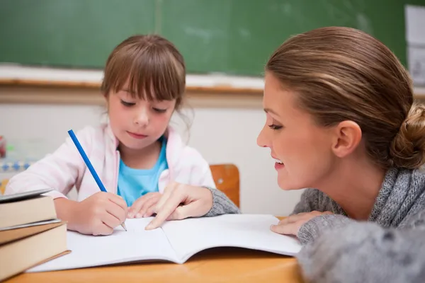 Roztomilá školačka psaní chvíli její učitel mluví — Stock fotografie