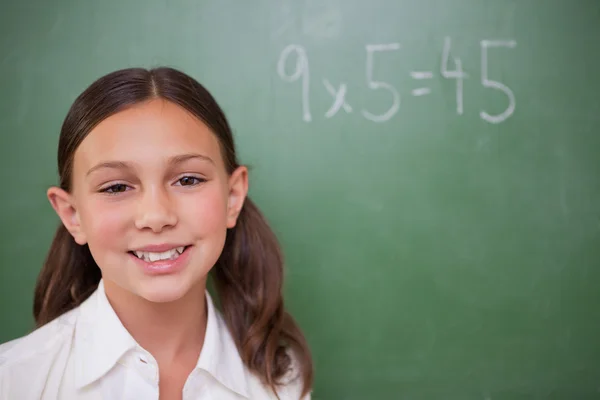 Glimlachend schoolmeisje poseren voor een schoolbord — Stockfoto