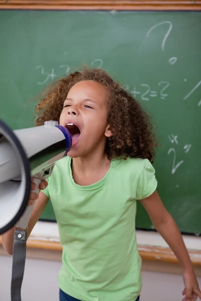 Portrait of a cute schoolgirl screaming through a megaphone — Stock Photo, Image