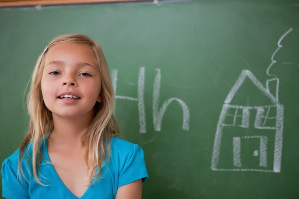 Blonde schoolgirl posing in front of a blackboard — Stock Photo, Image