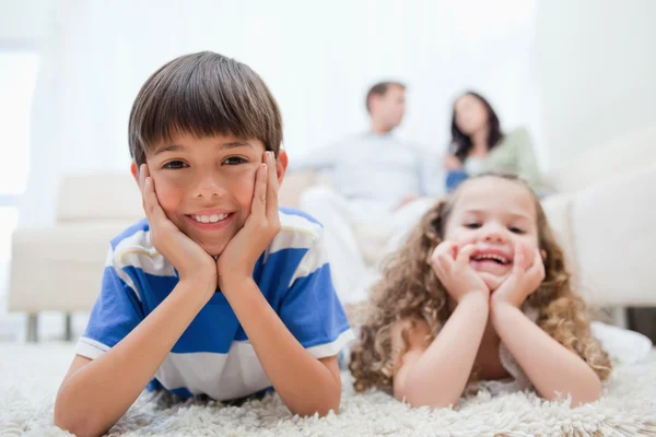 Çocuklar ebeveynleri ile halı üzerinde onların arkasında oturan yalan — Stok fotoğraf