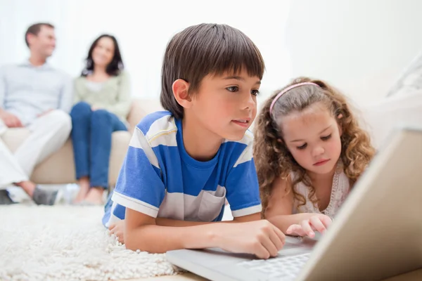 Enfants utilisant un ordinateur portable sur le tapis avec des parents derrière eux — Photo