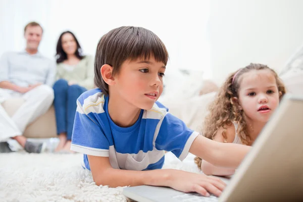 Enfants jouant à des jeux informatiques sur le tapis avec les parents derrière th — Photo