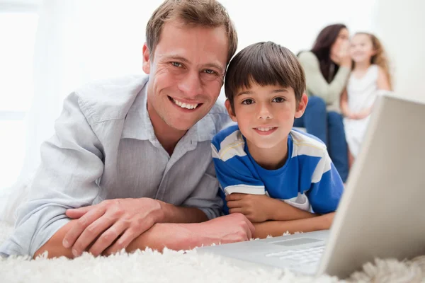 Smiling son and dad using laptop on the carpet — Stock Photo, Image