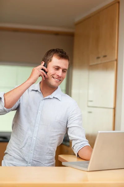 Masculino com celular e laptop na cozinha — Fotografia de Stock