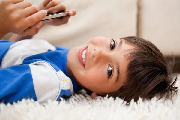 Pojken låg på mattan med mobiltelefon — Stockfoto