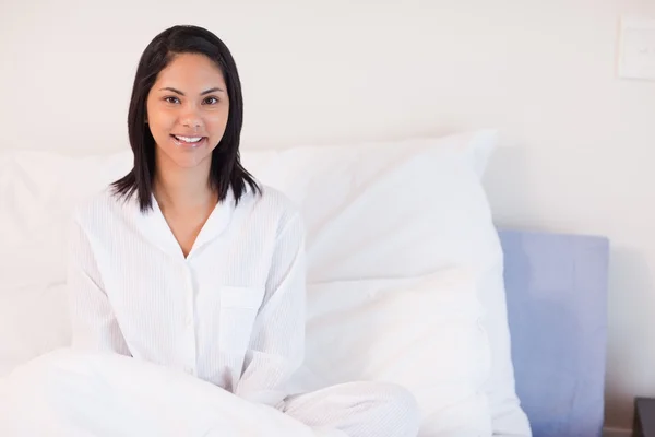Sorridente donna in pigiama seduta sul suo letto — Foto Stock