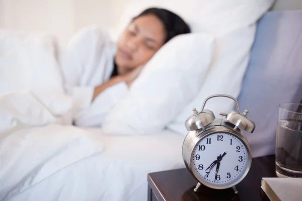 Reloj despertador junto a la mujer durmiendo en su cama — Foto de Stock