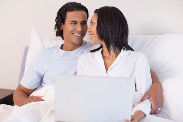 Jovem casal sentado na cama com seu laptop — Fotografia de Stock