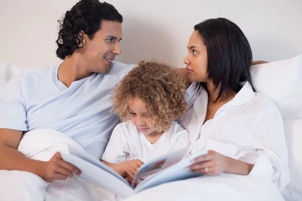 Family sitting on the bed reading a book — Stock Photo, Image