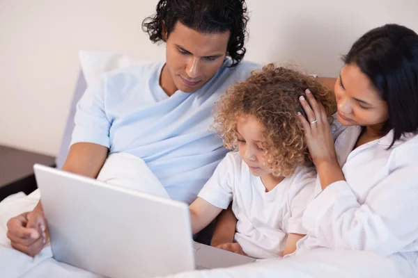 Family with laptop sitting on the bed — Stock Photo, Image