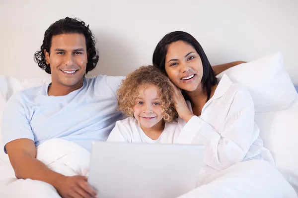 Семья сидит на кровати с ноутбуком — стоковое фото