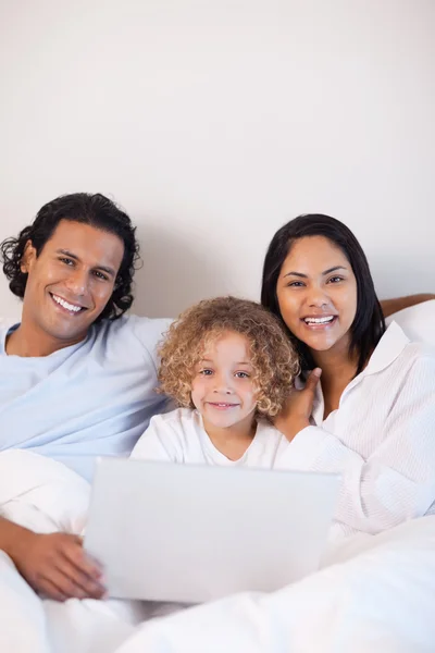 Familjen sitter på sängen med anteckningsboken tillsammans — Stockfoto