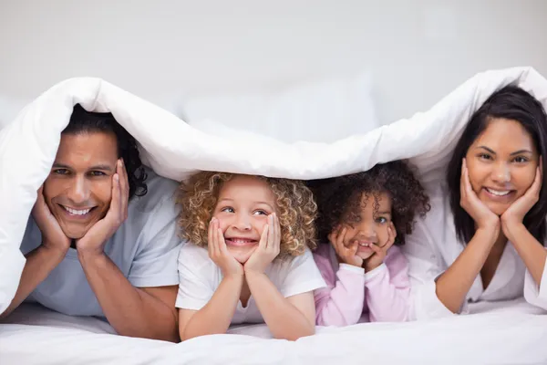 Sorrindo família escondida sob o cobertor — Fotografia de Stock
