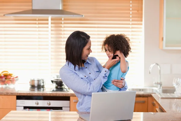 Mère et fille utilisant un ordinateur portable et un téléphone portable dans la cuisine pour — Photo