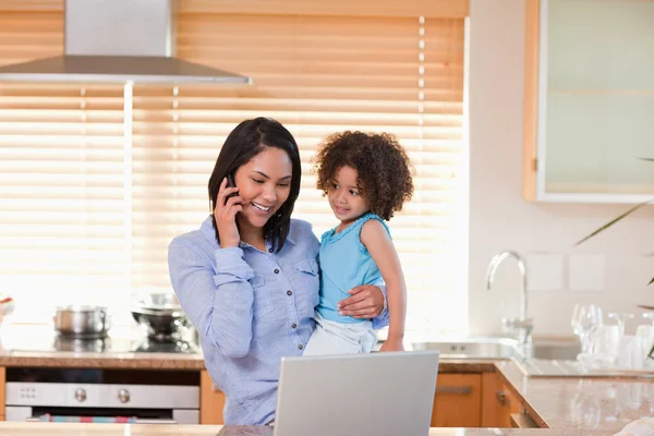 Madre e hija usando el teléfono celular y el portátil en la cocina para —  Fotos de Stock