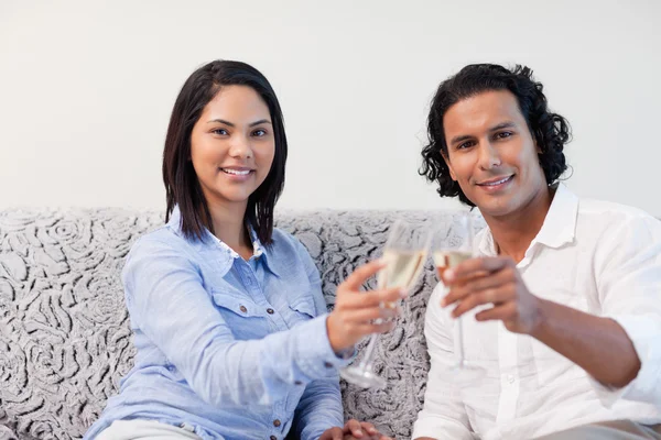 Casal comemorando com vinho espumante no sofá — Fotografia de Stock